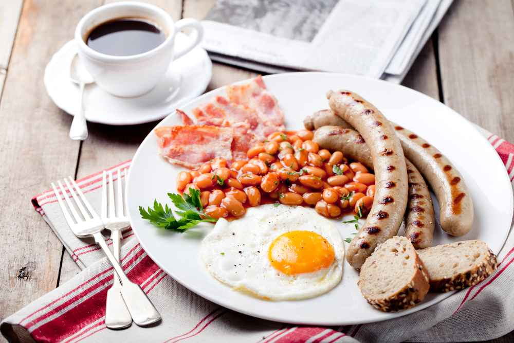 Fried egg with beans in tomato sauce, bacon and grilled sausages with a cup of coffee and morning newspaper © Anna_Pustynnikova / Shutterstock