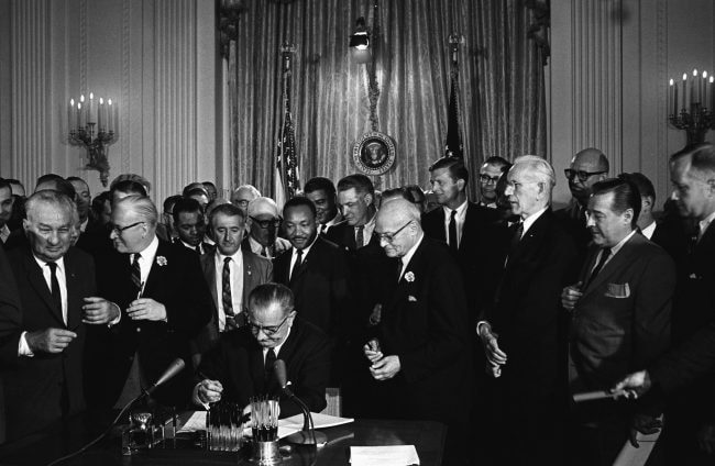 Lyndon Johnson signing the Civil Rights Act, 2 July 1964. Martin Luther king Jnr. looks on behind the President