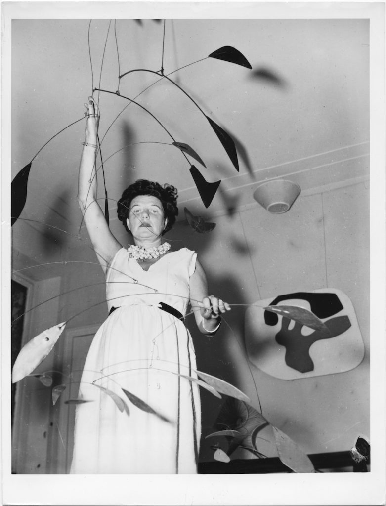 Peggy Guggenheim at Palazzo Venier dei Leoni with Alexander Calder, Arc of Petals (1941, PGC), Venice, early 1950s. Solomon R. Guggenheim Foundation. Photo Archivio CameraphotoEpoche. Gift, Cassa di Risparmio di Venezia, 2005 Behind her Jean Arp, Overturned Blue Shoe with Two Heels Under a Black Vault (1925, PGC).