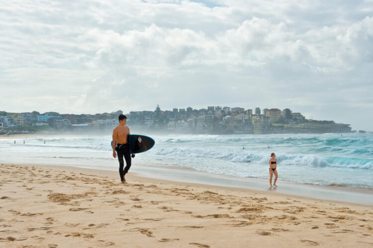 Surfer with board and woman in bikini strolling on Bondi beach