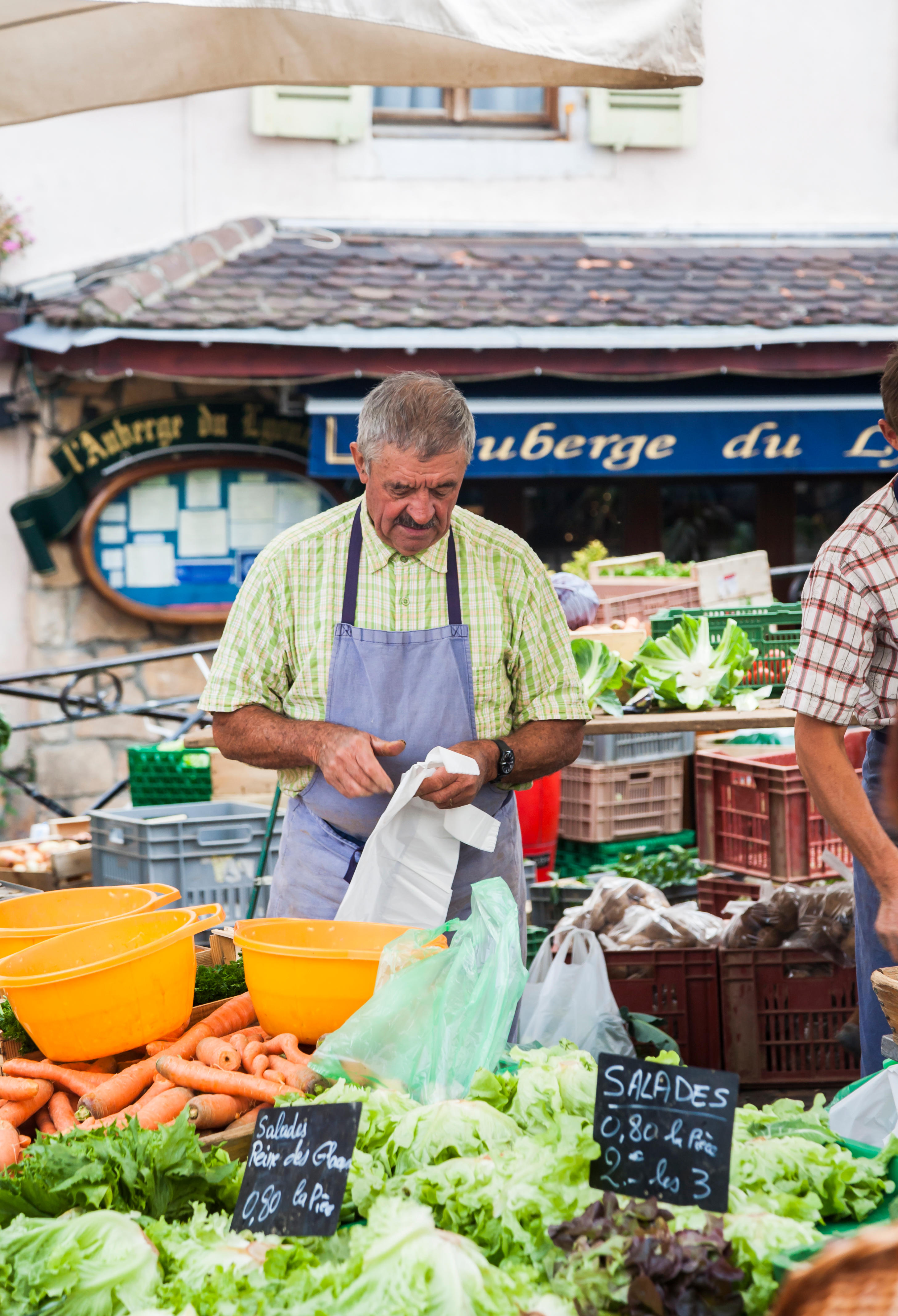 Male stallholder at a vegetable and salad stall at a local outdoor food market in the old town, Annecy, France