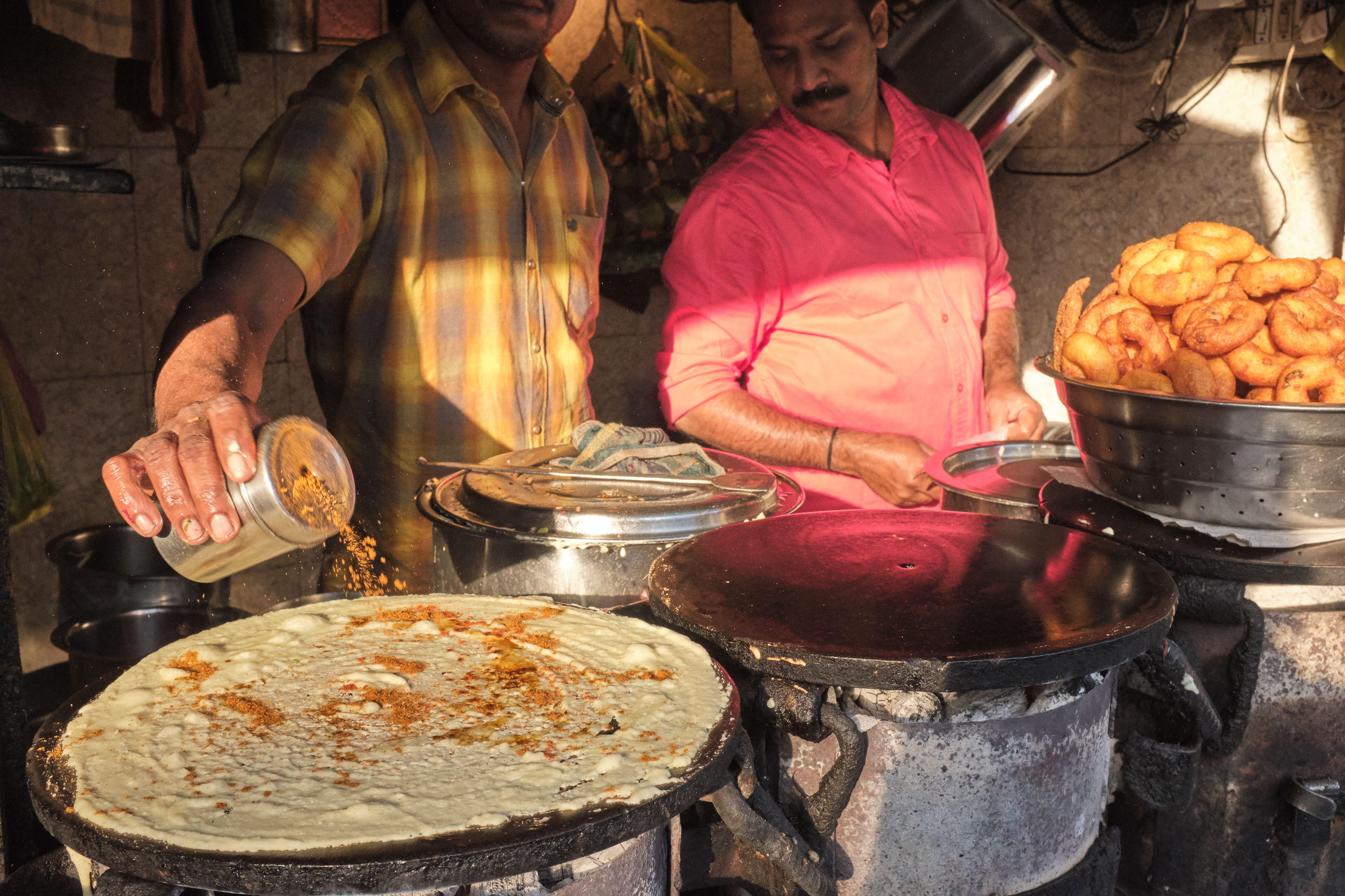 At a food stall in Mumbai, India, a cook makes Masala Dosa, a popular Indian dish, sprinkling spices on the batter. Right: a bowl of Vade / Vadas