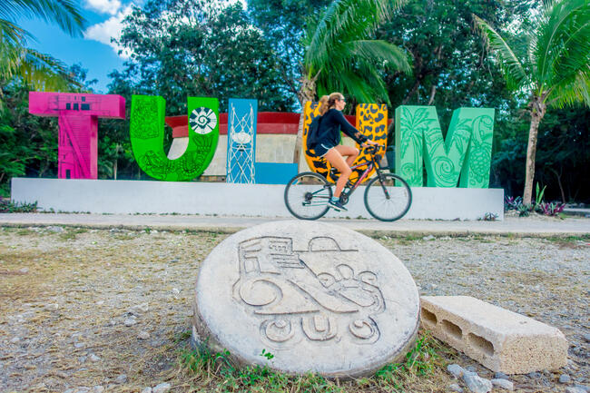 TULUM, MEXICO - JANUARY 10, 2018: Outdoor view of unidentified woman biking next to huge colorful letters Tulum at the enter of Mayan Ruins of Tulum in Meixco