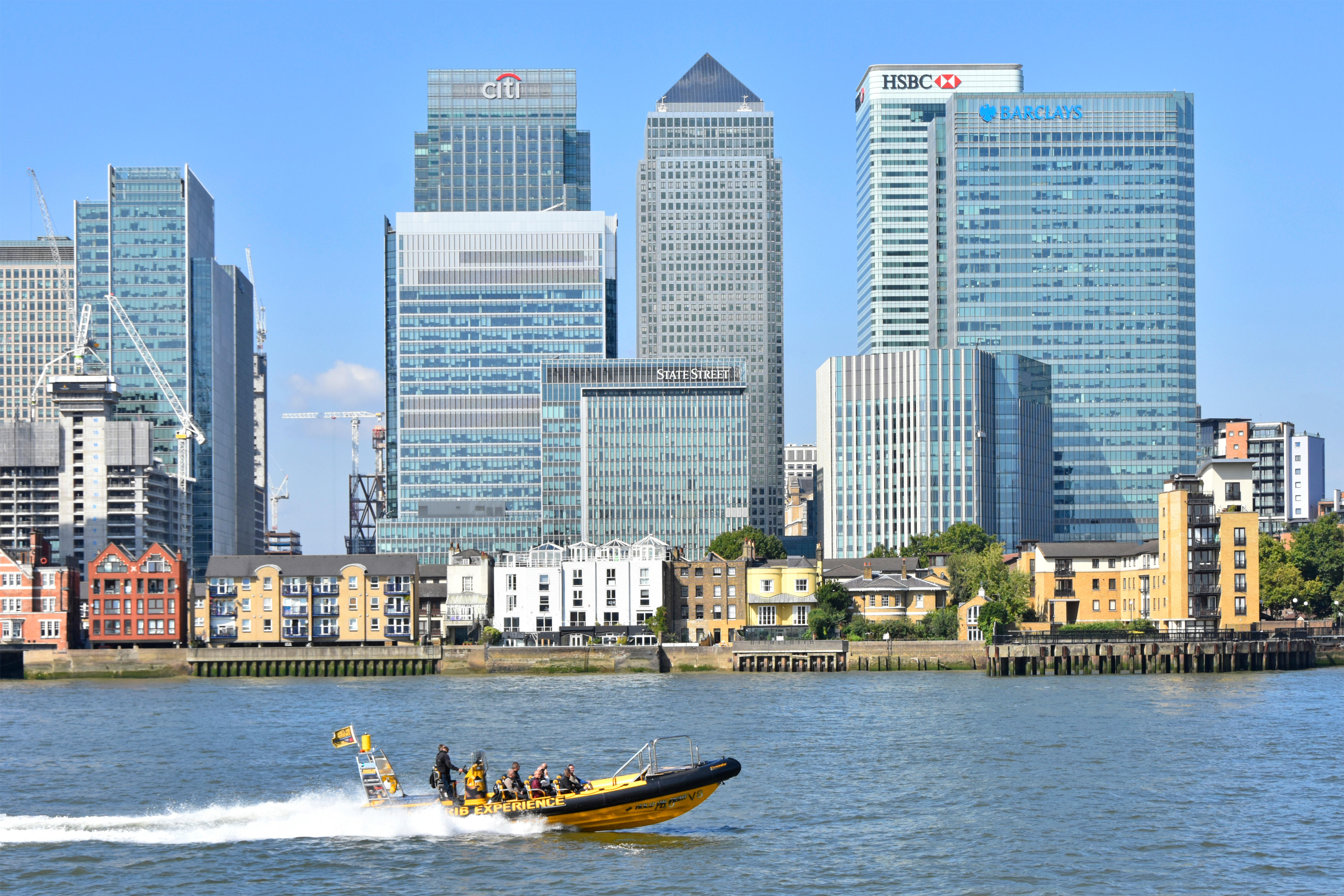 Thames Rib Experience tourists speedboat passing modern landmark skyscraper buildings on Canary Wharf Isle of Dogs London Docklands skyline England UK