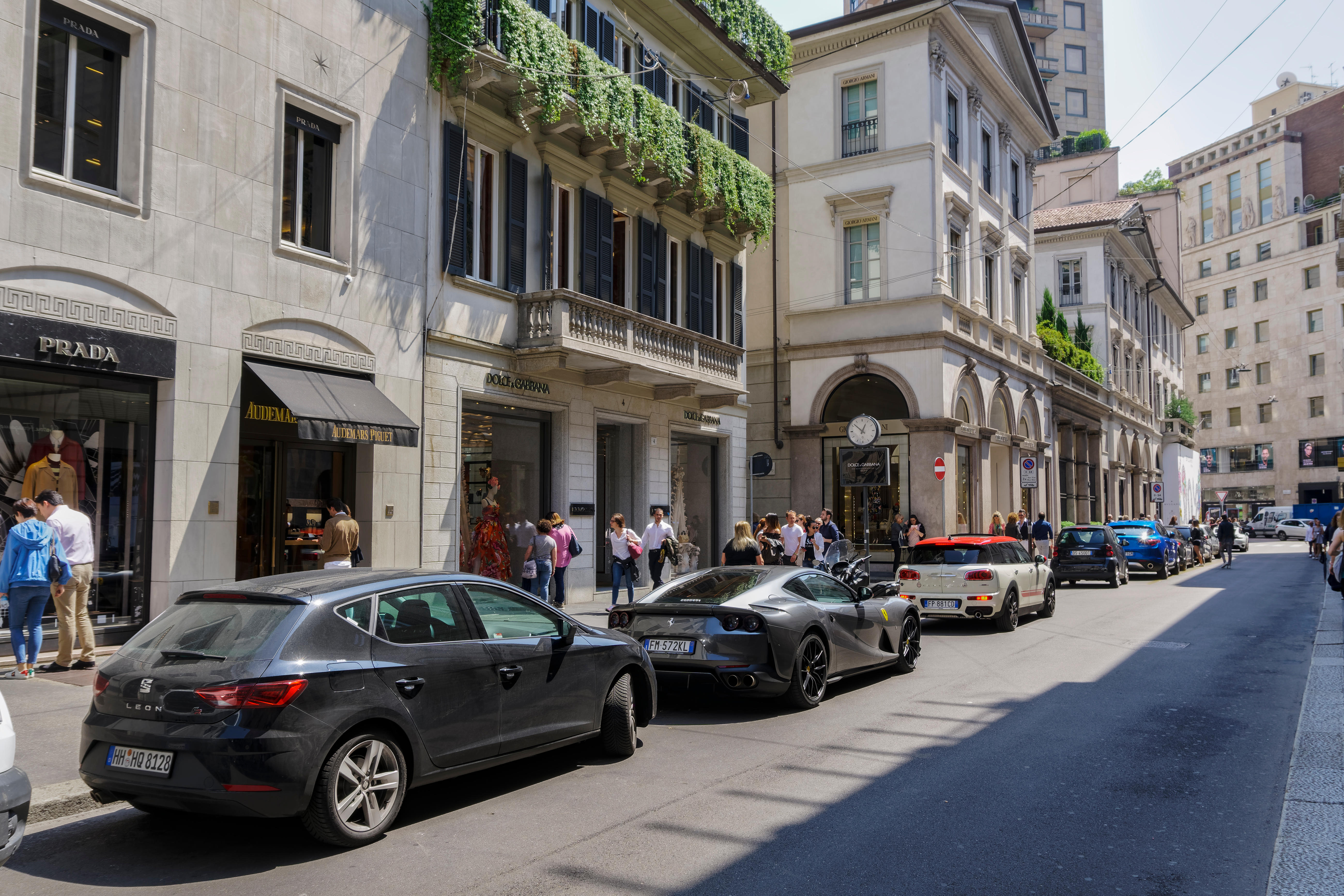 Milan Via Monte Napoleone upscale shopping street with luxury cars. People outside Milano fashion district Dolce & Gabbana high end exclusive boutique