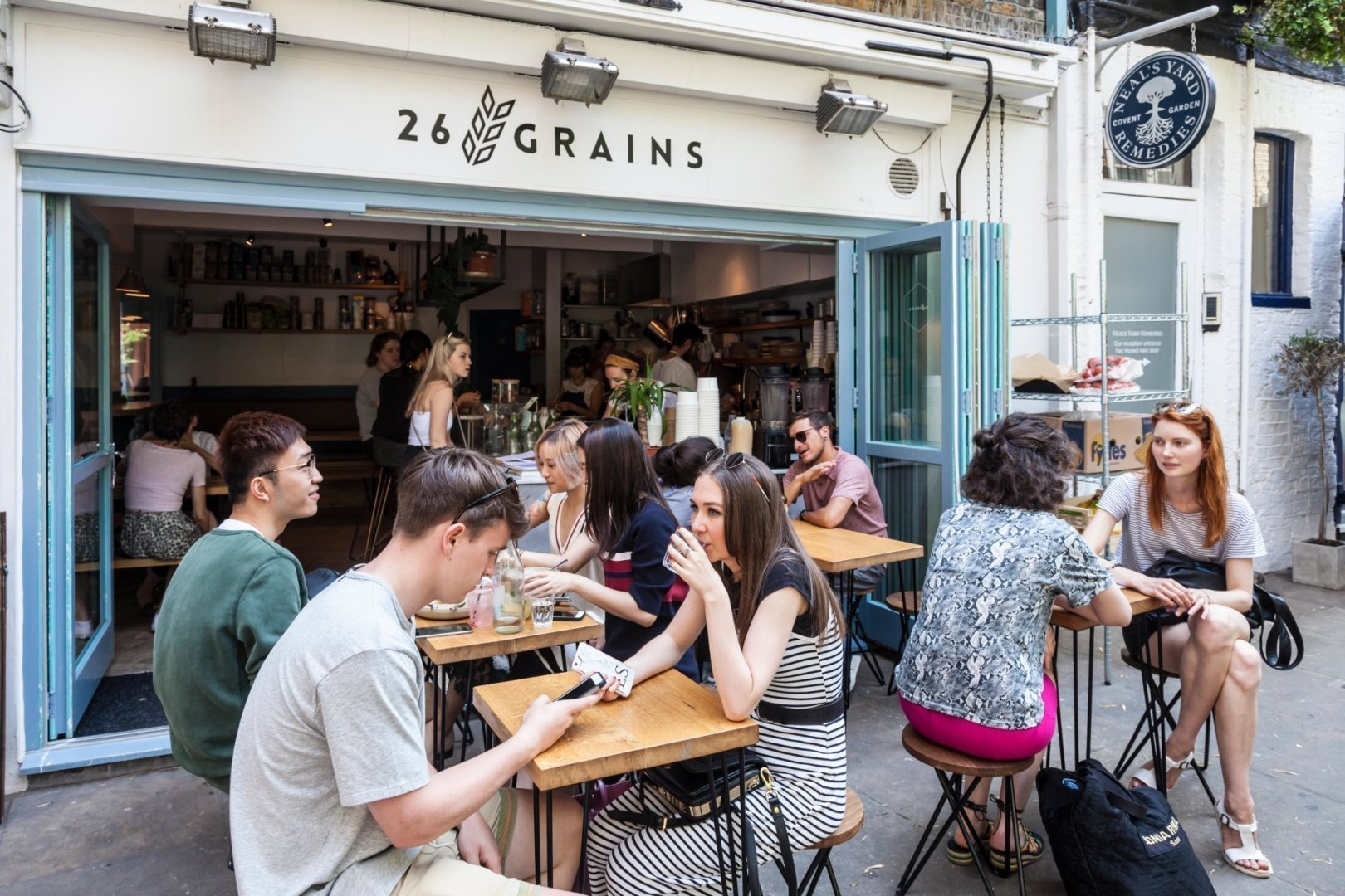 Clients sitting, relaxing, chatting, drinking in Neal's Yard courtyard, outside 26 Grains restaurant. Seven Dials, London, England, UK